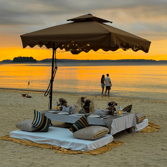 A shaded cabana setup on the beach with floor cushions and low tables, with 2 people standing near the shoreline at Silver Sand Sea Princess Beach Resort, Port Blair.